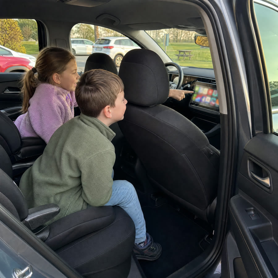 Zwei Kinder zeigen im geparkten Auto auf das Display